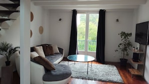 Een moderne woonkamer met een bank, een ronde glazen tafel, een televisie en een balkon met gordijnen.
