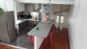A modern kitchen with a grey countertop, red stools, stainless steel appliances, and a grey pendant light.