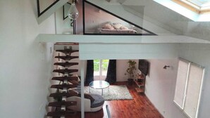 Ein modernes Interieur mit Treppe, Glasdach, Bett, rundem Tisch und Zimmerpflanze.
