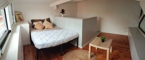 Een slaapkamer met een bed, een klein tafeltje, een potplant en een raam.