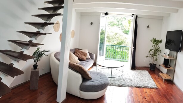 Ein modernes Wohnzimmer mit einer Wendeltreppe, einem Sofa, einem kleinen runden Tisch und einem Fernseher.