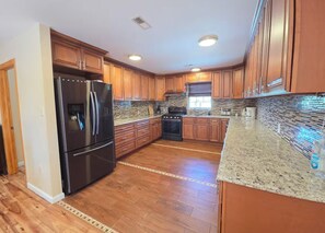 A kitchen with wooden cabinets, a stainless steel refrigerator, a stove, and granite countertops. - Elberon Escape-4BR Stay Near Bay,10 Min to Casinos (Atlantic City)