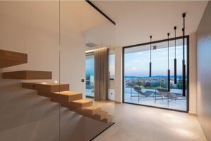 Ein modernes Interieur mit einer Treppe, einer Glastür, die auf einen Balkon mit Aussicht führt, und einem minimalistischen Design.