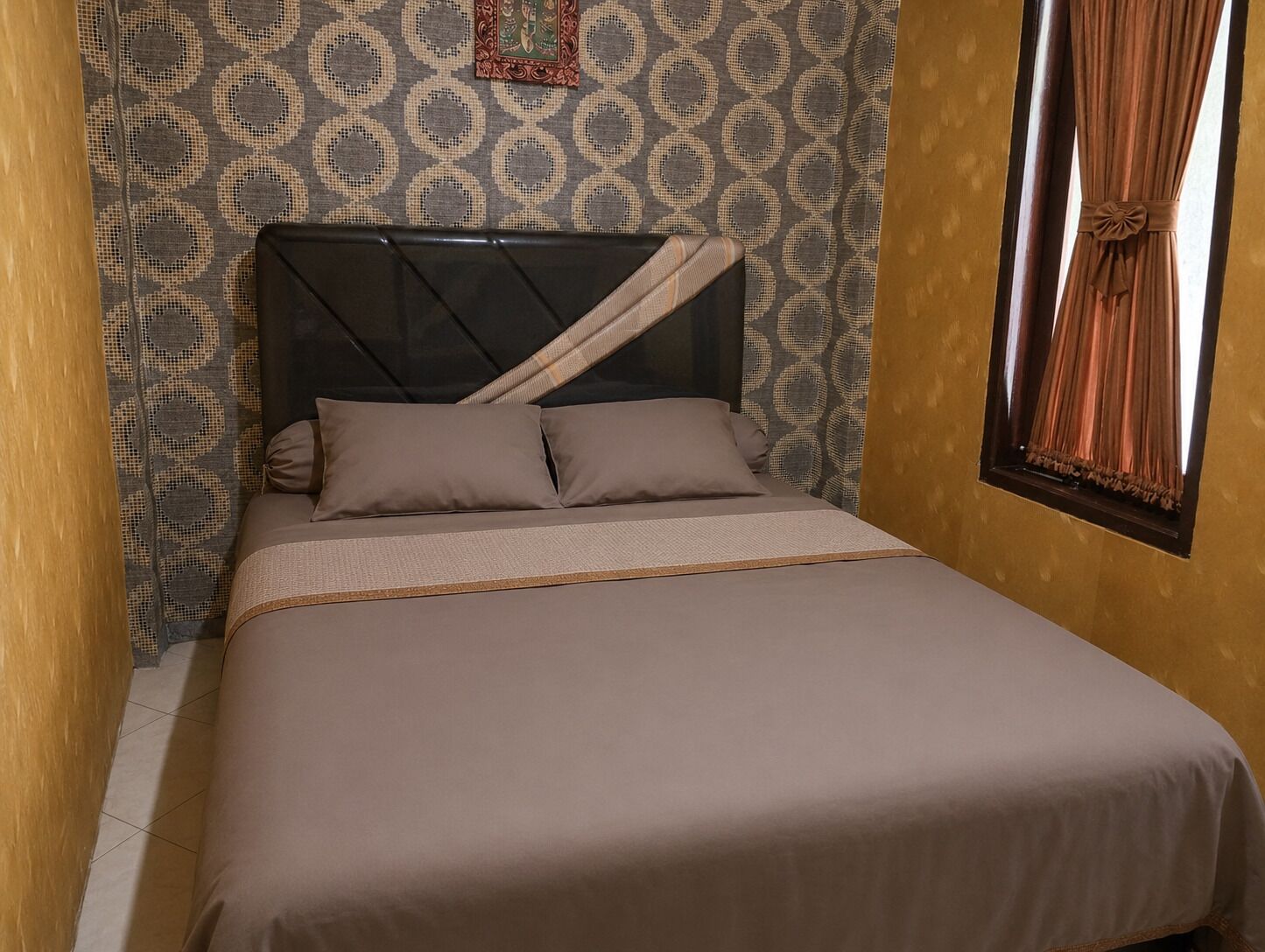 Uma cama de solteiro com cabeceira, parede estampada e janela com cortinas.