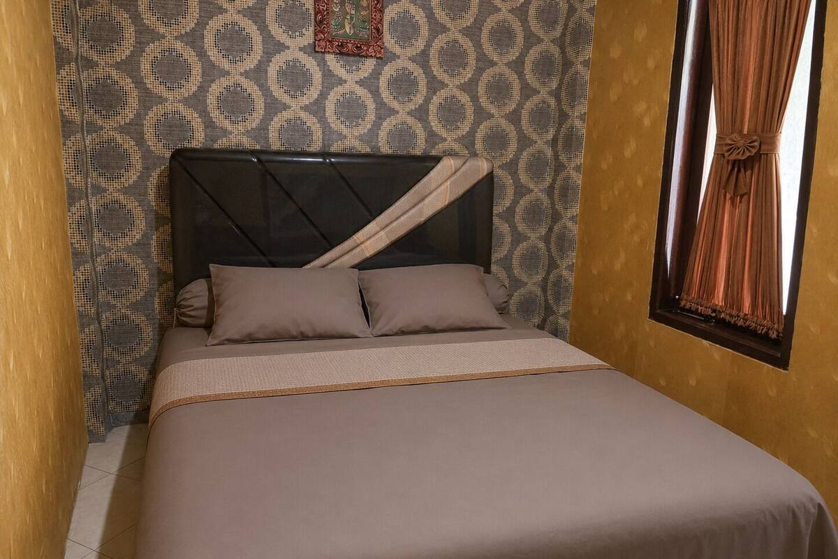 Una cama individual con cabecera, pared estampada y ventana con cortinas.