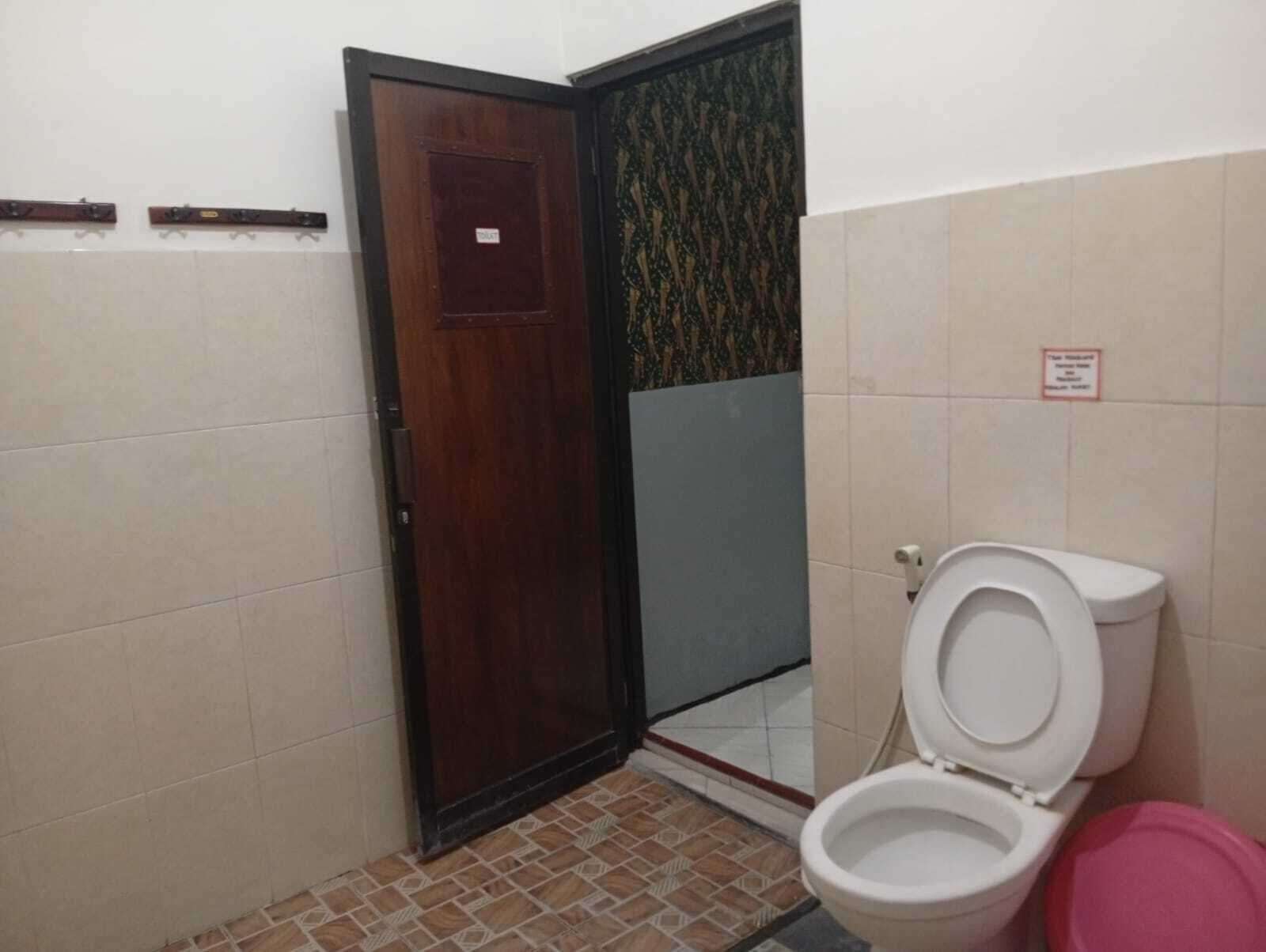 A small bathroom with a toilet, a wooden door, and a tiled floor.