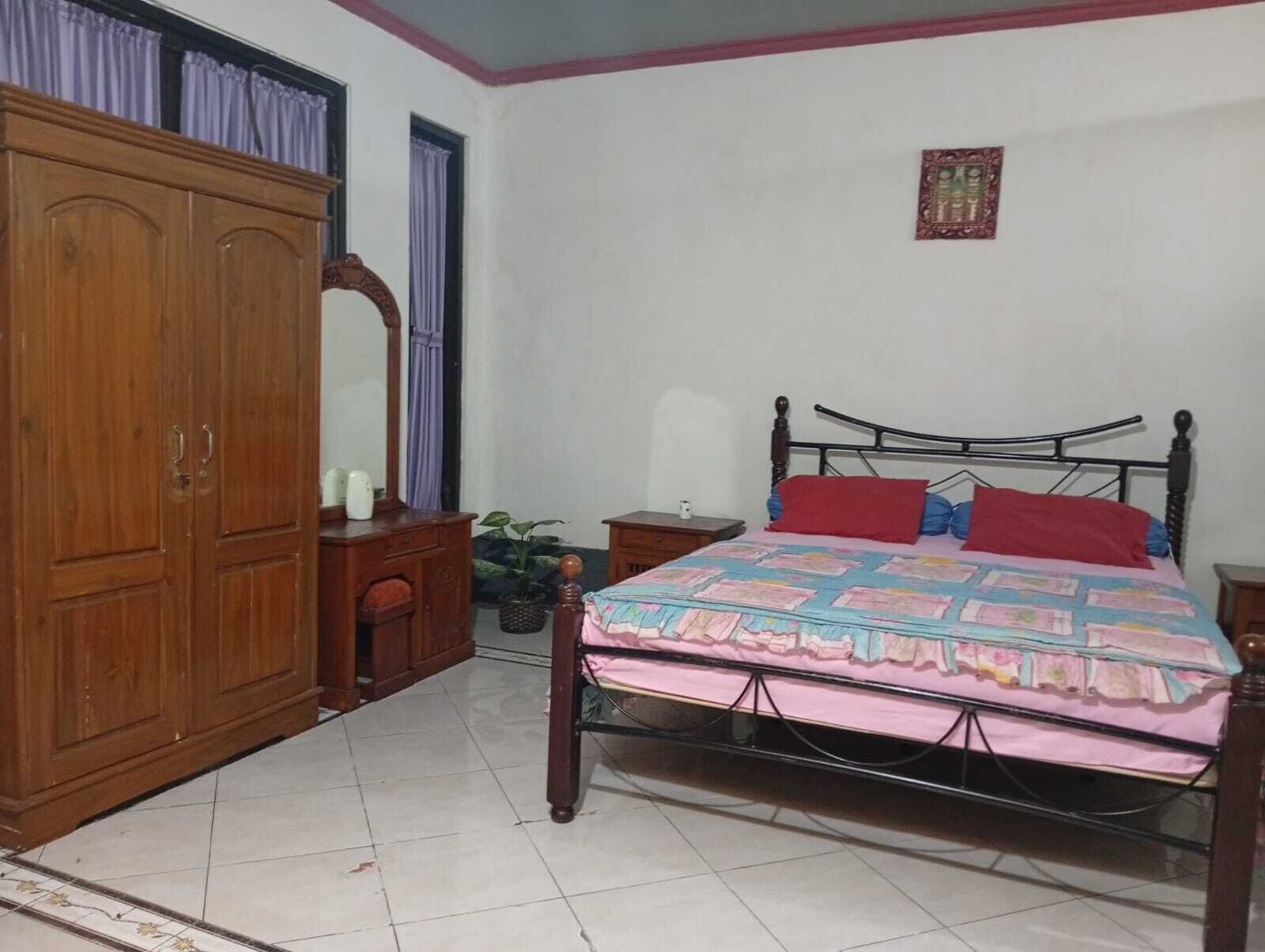 Quarto com cama, guarda-roupa de madeira e uma pequena mesa com uma planta.