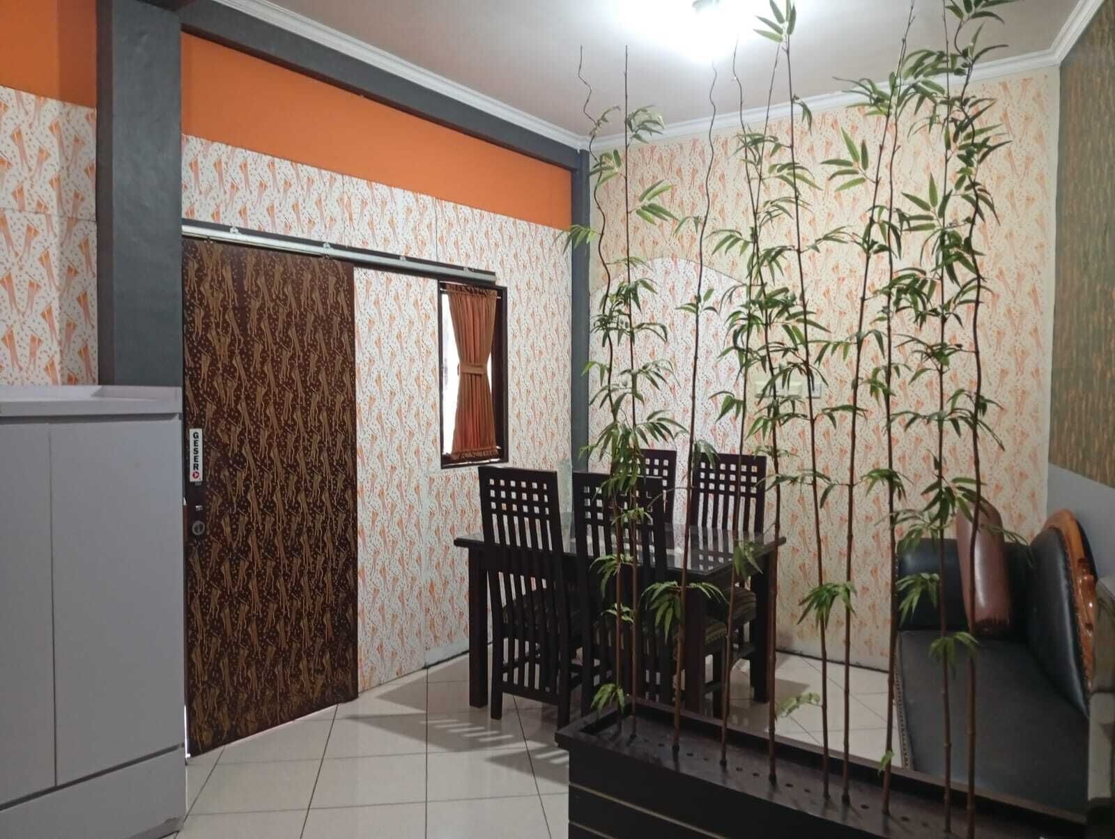Una habitación con suelo de baldosas, una puerta con papel pintado estampado, una ventana con cortinas, una mesa de comedor con sillas y varias plantas altas.