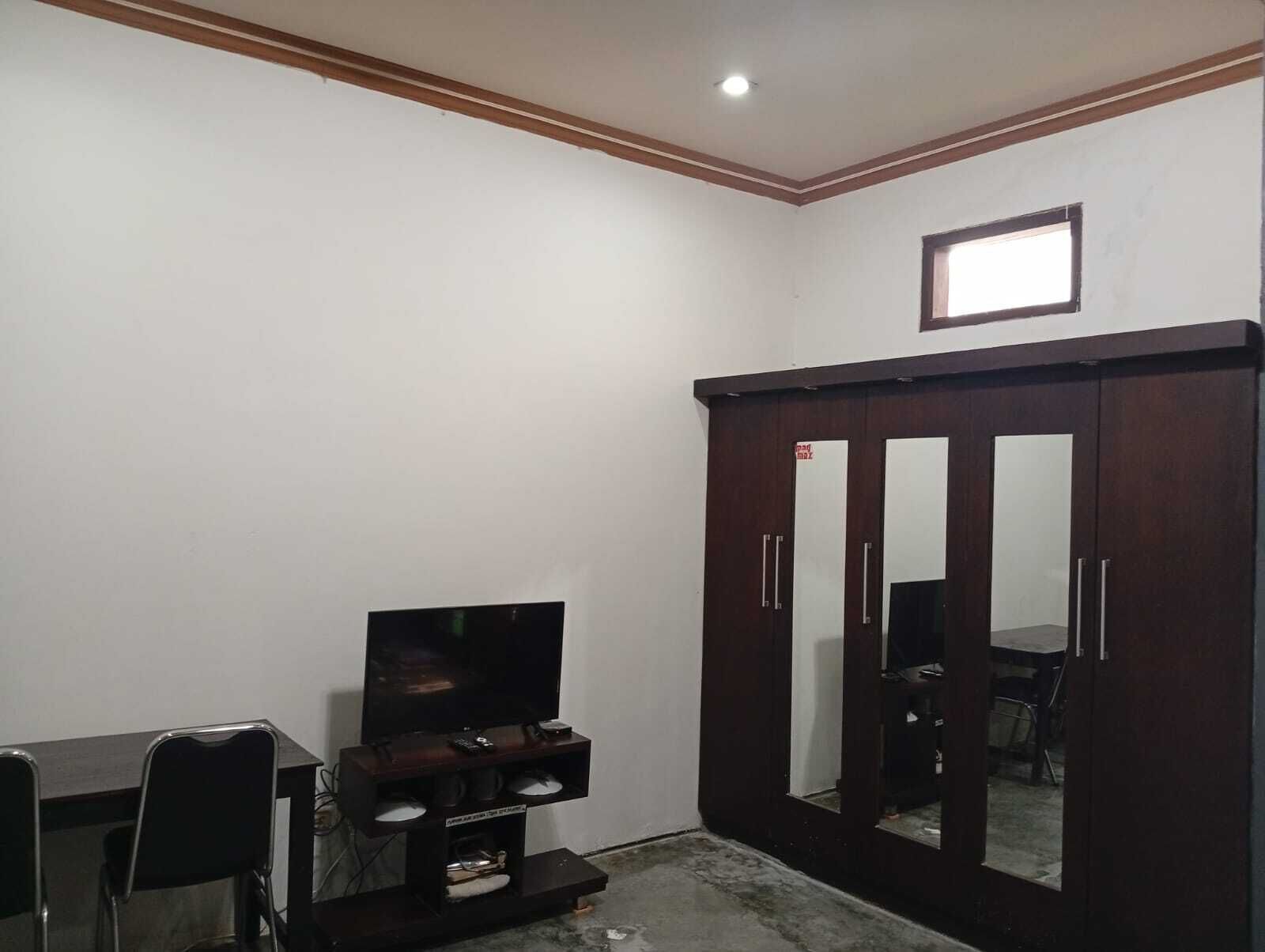 A room with a dark wooden wardrobe, a television on a stand, and a small table with chairs.