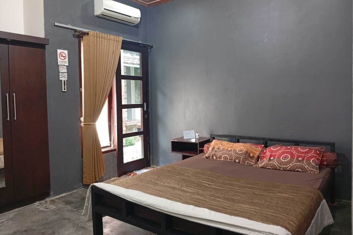 Un dormitorio con cama, mesita de noche, armario, equipo de aire acondicionado y ventana con cortinas.