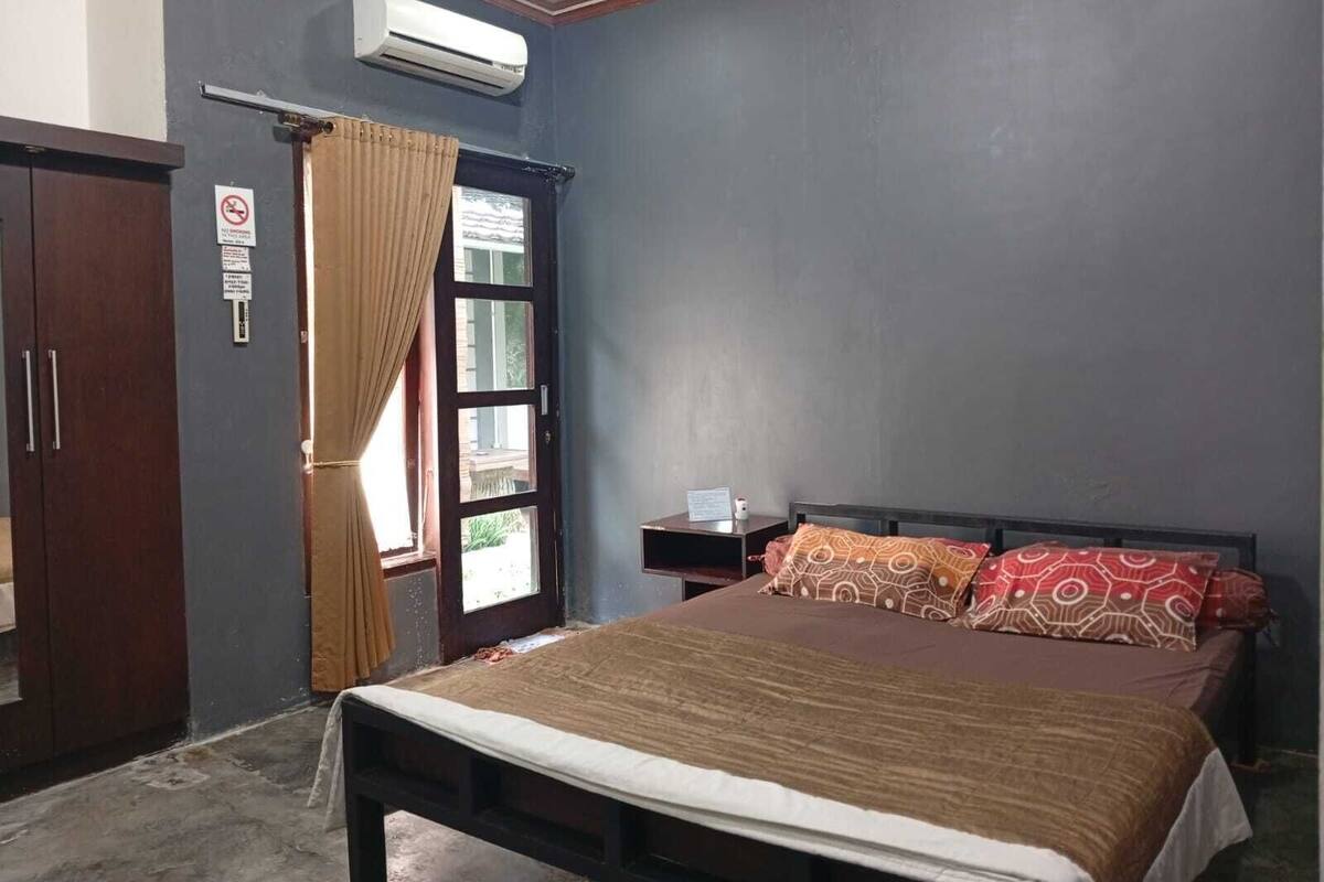 A bedroom with a bed, a nightstand, a wardrobe, an air conditioning unit, and a window with curtains.