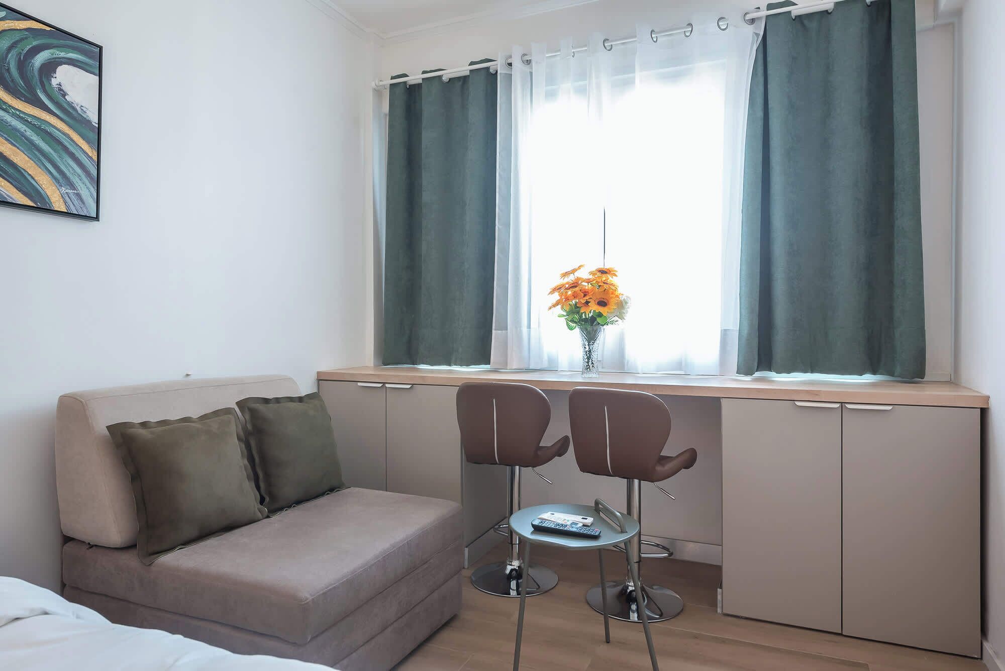 A room with a sofa, two chairs, a desk, and a window with curtains.