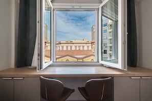 A room with a large window, two chairs, and a view of a building with red-tiled roofs. - Stylish Studio KingBed&Workspace-WkndNse (Athina)