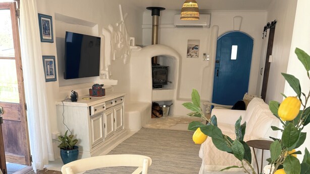 Zona pranzo con tavolo di legno apparecchiata per un pasto, una televisione sullo sfondo e una porta blu.