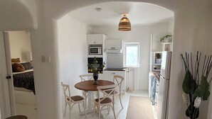 Una cucina compatta con mobili bianchi, un tavolo da pranzo con sedie, un lampadario e un frigorifero.