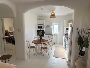Ett kompakt kök med vita skåp, ett matbord med stolar, en hängande lampa och ett kylskåp.