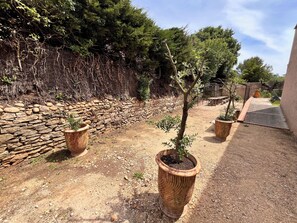 Un jardin agrémenté de plantes en pot, d’un mur en pierre et d’une zone dallée.