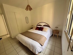 Une chambre à coucher comprenant un lit, des tables de chevet, un luminaire suspendu, une armoire et une fenêtre.