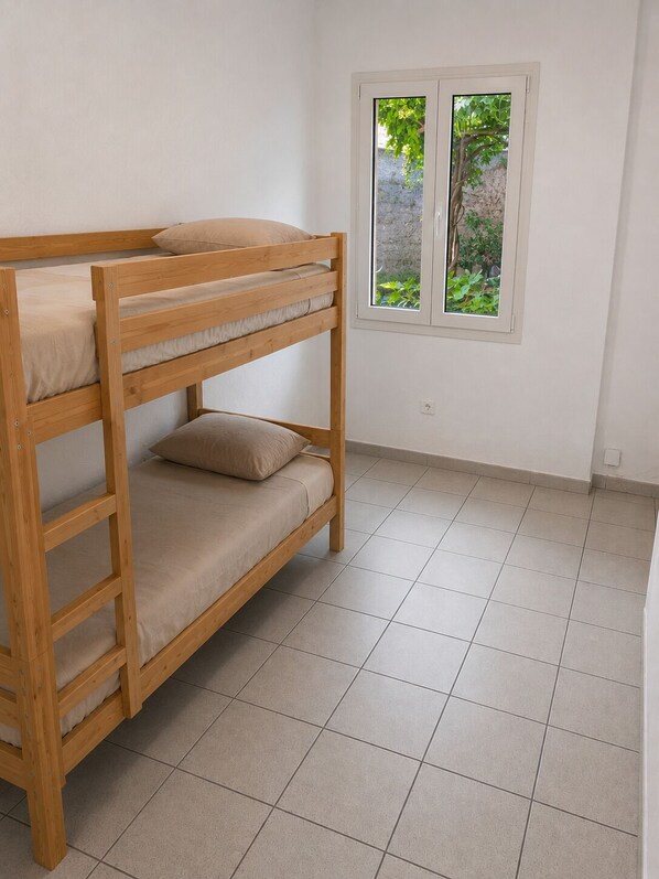 Una cama individual superpuesta con ventana, paredes blancas y suelo de baldosas.