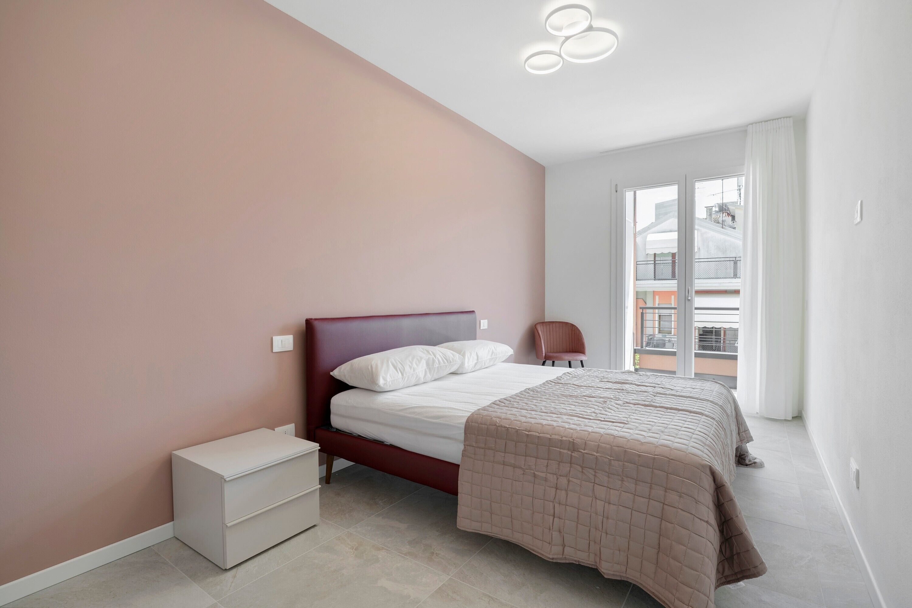 Ein Schlafzimmer mit einem Bett, einem Nachttisch, einem Sessel und Blick ins Freie.