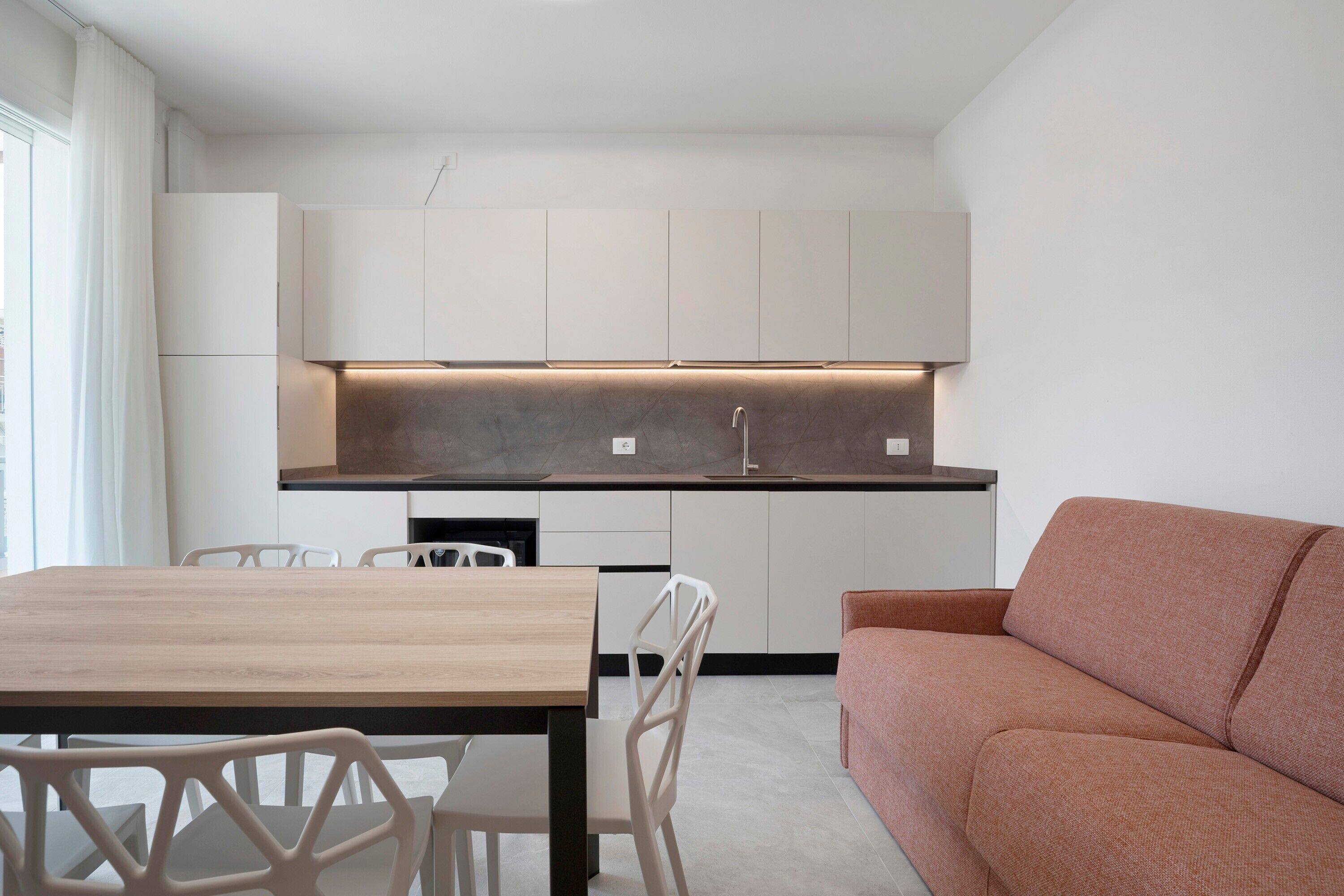 A modern kitchen with white cabinets, a wooden dining table, and a sofa.