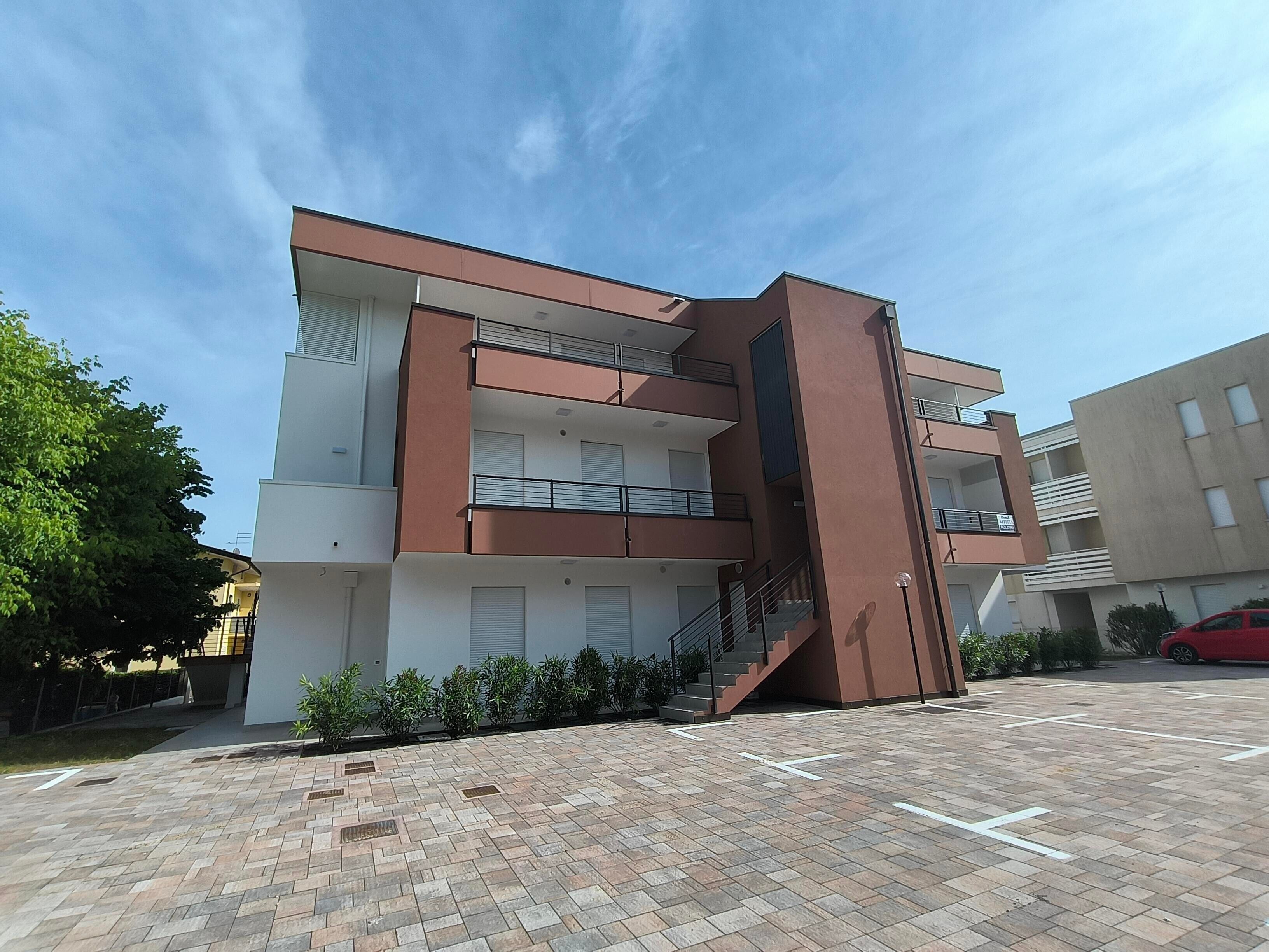A multi-story residential building with balconies, a staircase, and a parking area.