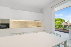 Eine moderne Küche mit weißen Schränken, einer Marmorarbeitsplatte und einem Essbereich mit Tisch und Stühlen.