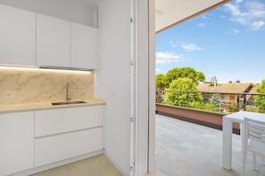 Eine moderne Küche mit weißen Schränken, einer Marmorarbeitsplatte und Blick auf einen Balkon mit Tisch und Stuhl.