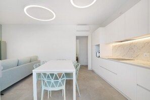 A modern kitchen with white cabinetry, a marble countertop, and a dining area with a white table and chairs. - Apartment 'Villa Luna 9' with Private Terrace, Balcony and Air Conditioning (Lido di Jesolo)