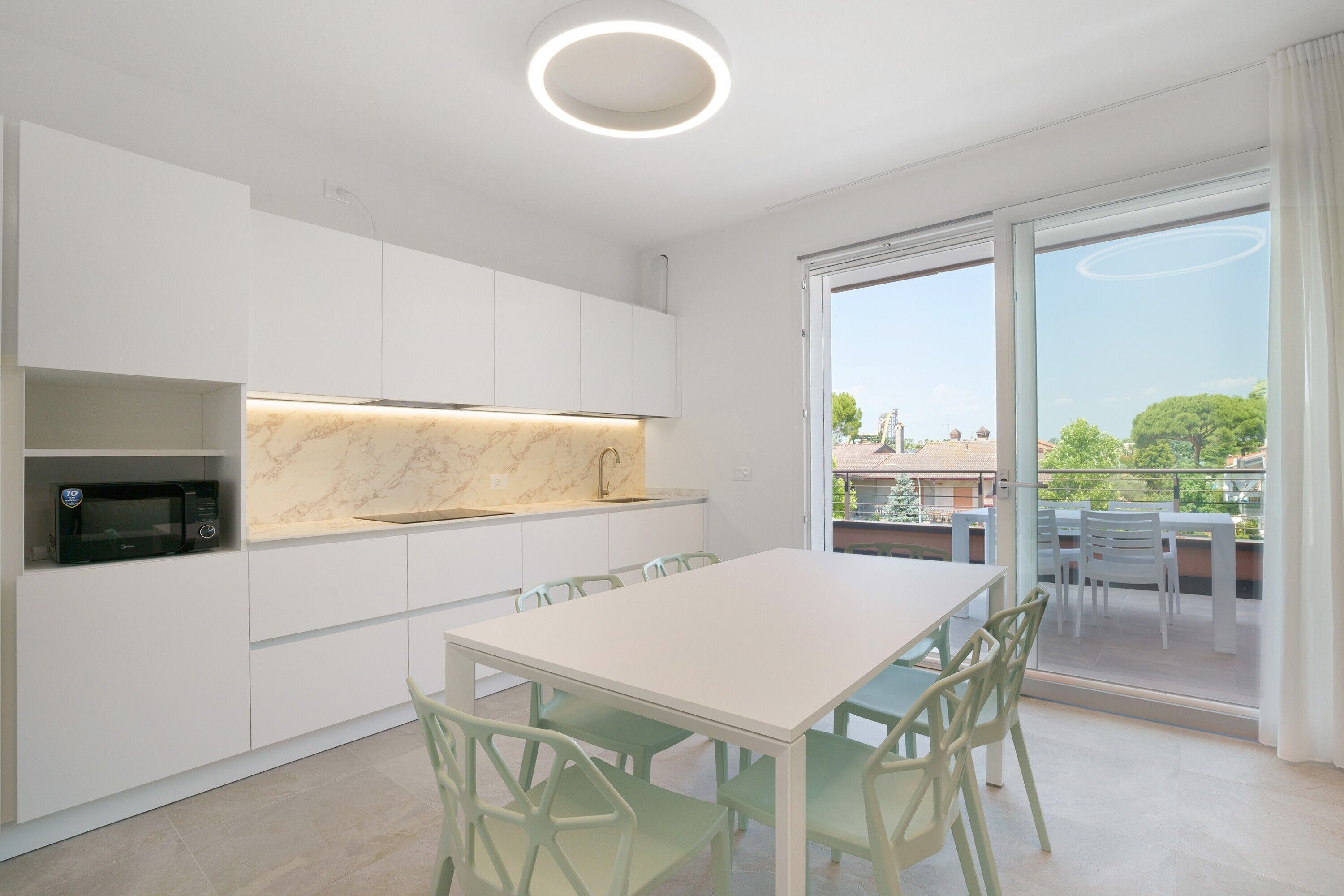 A modern kitchen with white cabinets, a marble countertop, and a dining area with a white table and green chairs.