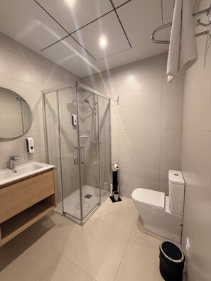Un baño moderno con ducha de vidrio, inodoro blanco y tocador de madera con espejo.