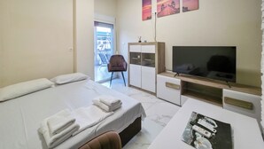 Ein Hotelzimmer mit Bett, Fernseher, Schreibtisch mit elektronischen Geräten, Stuhl und einem Kunstwerk an der Wand.