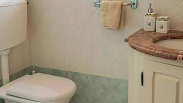 A bathroom with a toilet, a sink with a marble countertop, and a window with a geometric pattern.