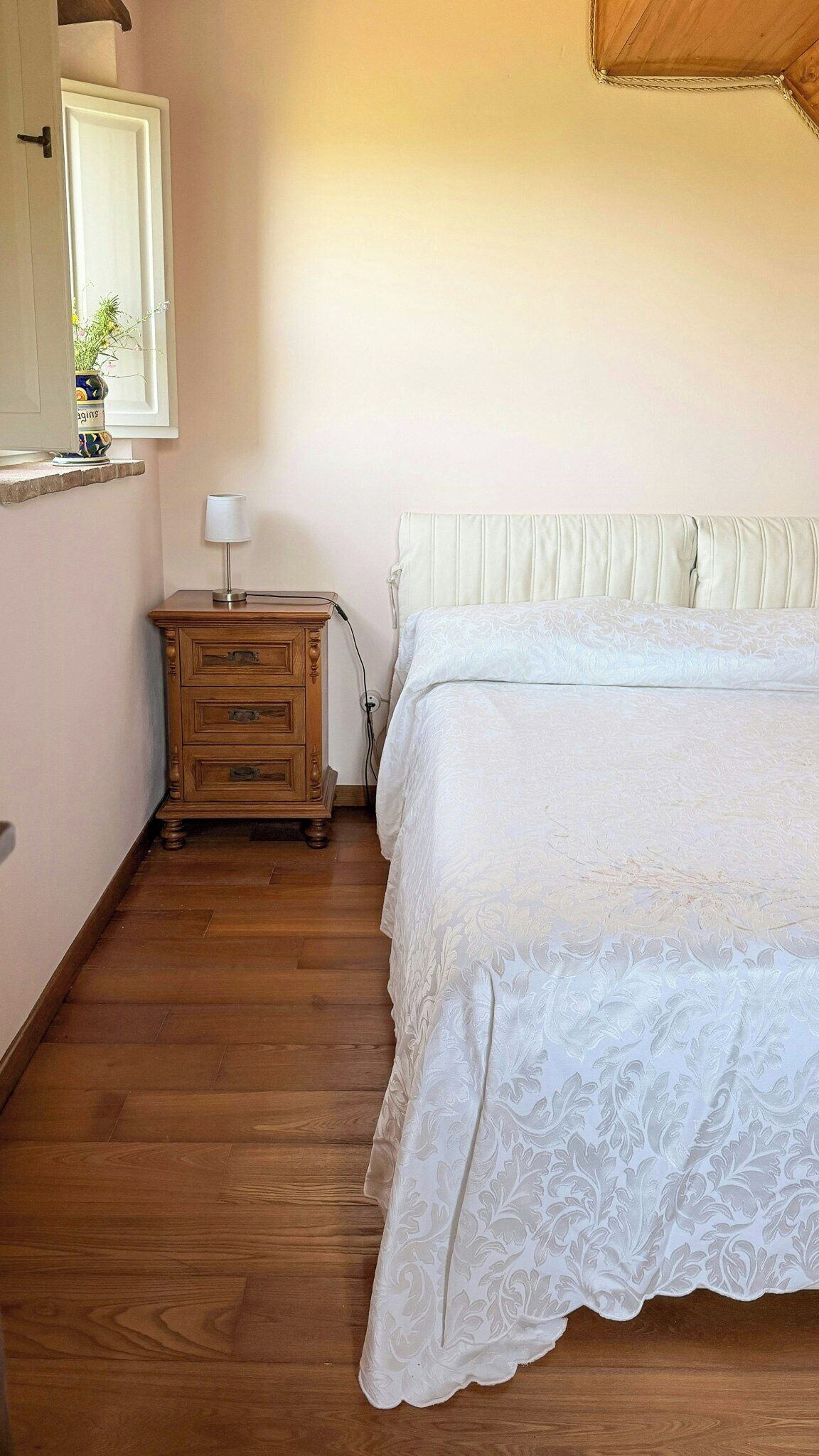 A bedroom with a wooden dresser, a bedside lamp, and a bed with a white headboard.