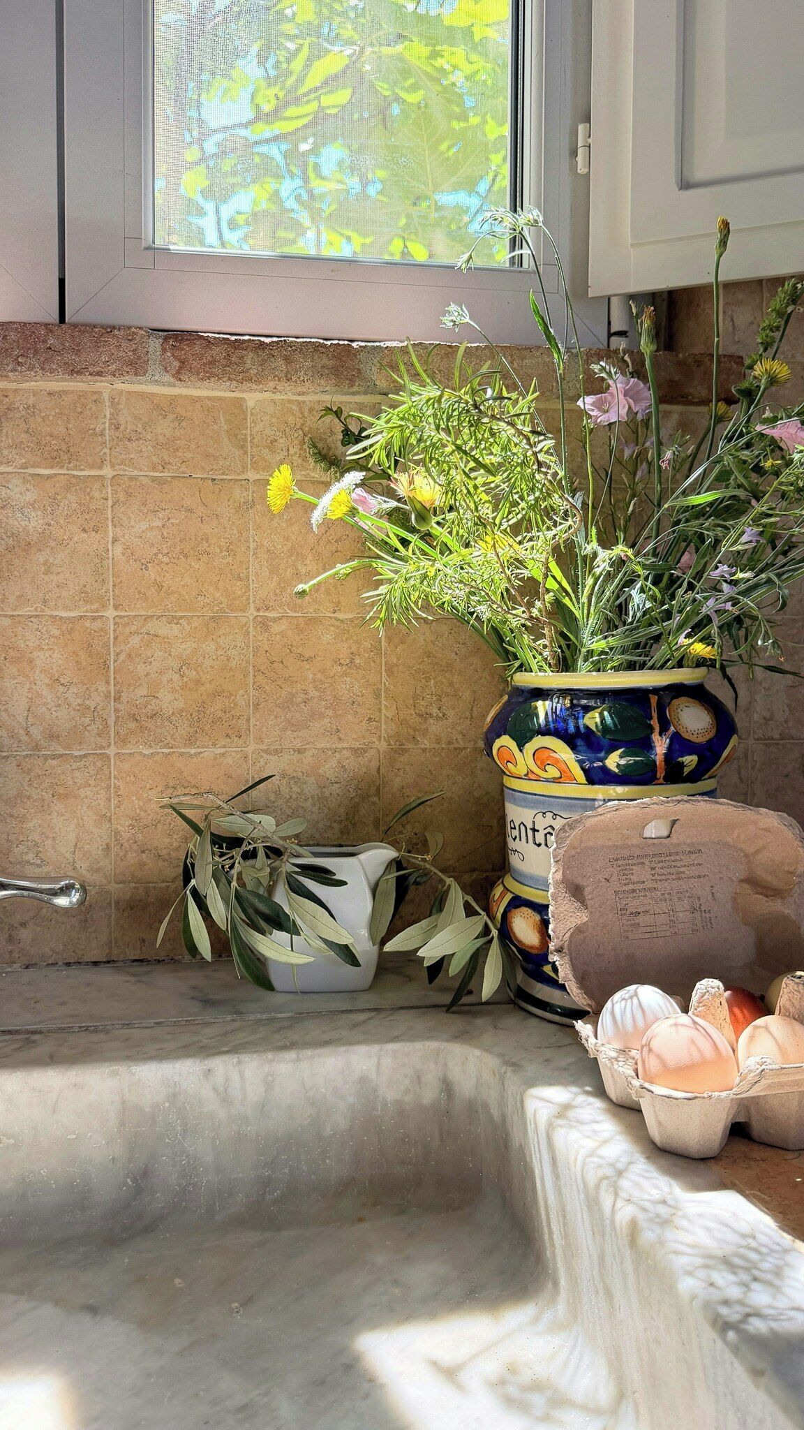 Eine Küche mit Spüle, einem Fenster mit Blick ins Grüne und einer dekorativen Vase mit Blumen.