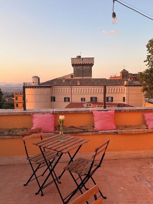 Eine Terrasse mit Tisch und Stühlen, eine Vase mit Blumen und Blick auf ein historisches Gebäude mit einem Turm.