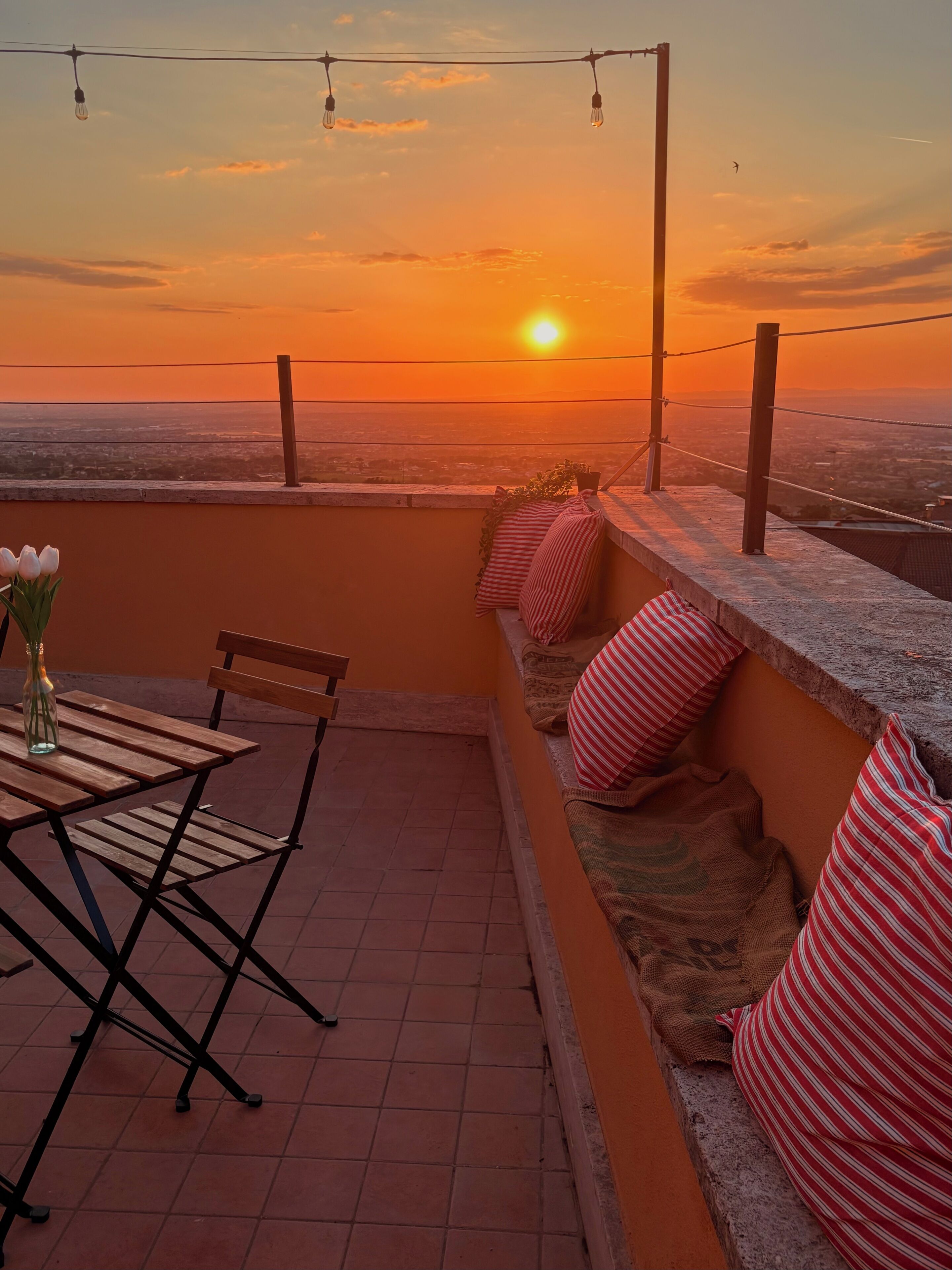 Um terraço com vista para o pôr do sol, uma mesa com cadeiras e um vaso de planta.