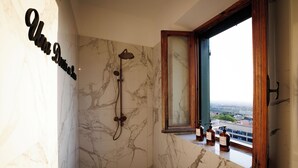 Casa de banho com chuveiro, janela com vista e parede de mármore.