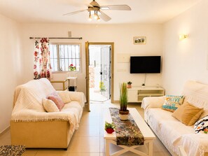 Ein Wohnzimmer mit zwei Sofas, einem Couchtisch, einem Fernseher und einer Tür, die nach draußen führt.