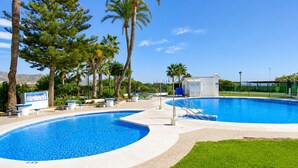 Une piscine entourée d’une terrasse, de palmiers et sous un ciel dégagé.