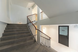 A staircase with a handrail, a door with a sign, and a light fixture on the wall. - Wachi Hotel (Songkhla)