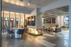 A modern hotel lobby with a checkered floor, a central round table with chairs, a reception desk, and artwork on the walls. - Wachi Hotel (Songkhla)