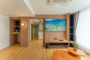 A modern hotel room with a large TV, wooden flooring, a small table, and a plant. - Wachi Hotel (Songkhla)