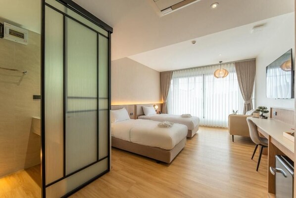 A hotel room with two beds, a desk, a chair, and a sliding door. - Wachi Hotel (Songkhla)