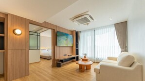 Una habitación de hotel moderna con suelo de madera, un sofá, una mesa de centro, un televisor y un cuadro en la pared.