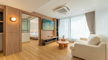 A modern hotel room with a wooden floor, a sofa, a coffee table, a TV, and a painting on the wall.
