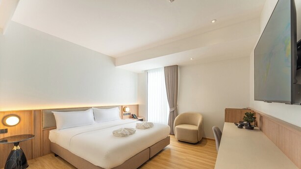 Una habitación de hotel moderna con una cama grande, mesitas de noche, un escritorio, una silla y un televisor montado en la pared.