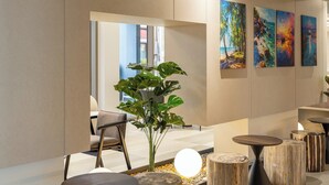 Un interior moderno con una zona de estar, una planta, taburetes de madera y una obra de arte en la pared.