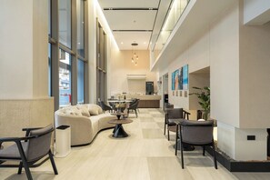 A modern hotel lobby with a curved sofa, a round table, and a bar area. - Wachi Hotel (Songkhla)