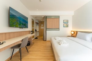 Habitación de hotel con cama, escritorio con silla, televisor montado en la pared y puerta que da a otra habitación.